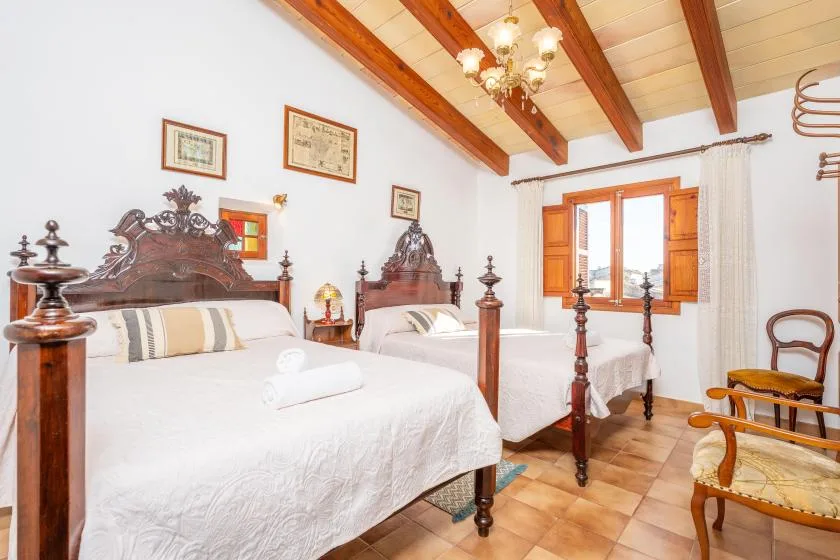 A bright bedroom with two beds and wooden ceiling beams.