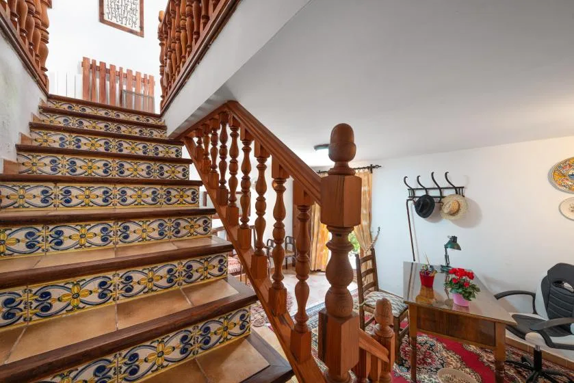 A tiled staircase with a wooden railing rises beside a small seating area.