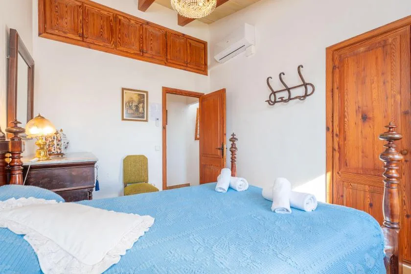 A bedroom with a blue bedspread, wooden doors, and a wall-mounted coat rack.