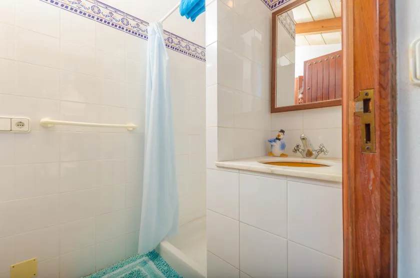 A tiled bathroom with a shower curtain and a sink beside a wooden door.