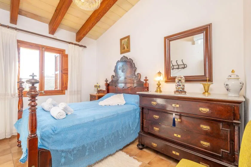 A bedroom with a blue-covered bed and a wooden dresser beside it.