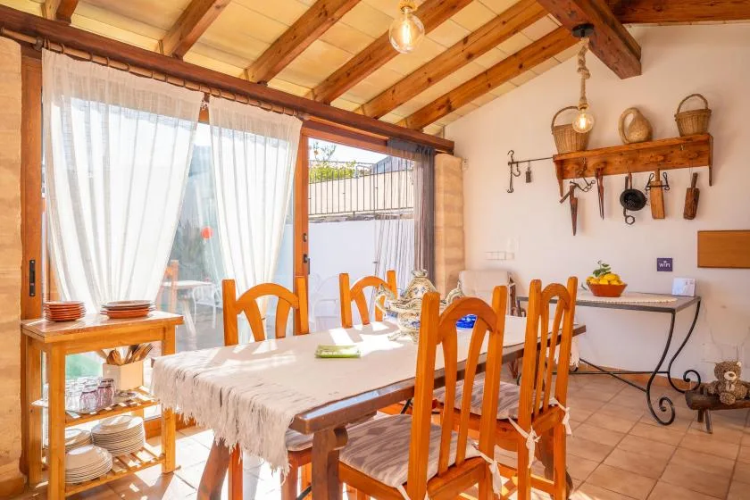 A bright dining area has a wooden table and chairs beside a curtained glass door.