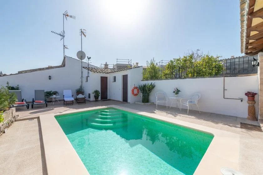 An outdoor swimming pool sits in a sunny courtyard with lounge seating.