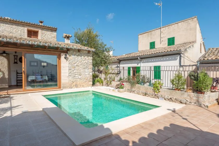 A swimming pool sits in a sunny courtyard beside stone and stucco buildings.