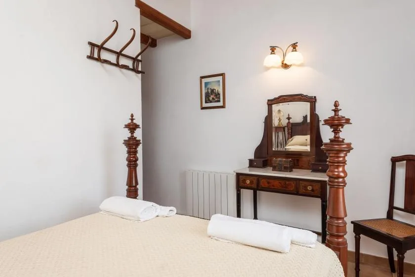 A bedroom with a wooden vanity and a bed topped with folded linens.