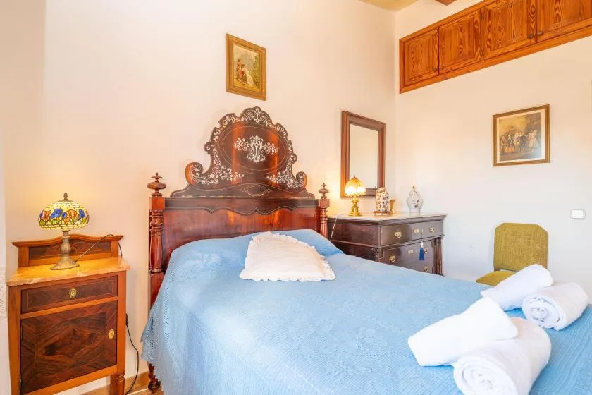 A bedroom with a carved wooden bed, blue bedding, and bedside furniture.