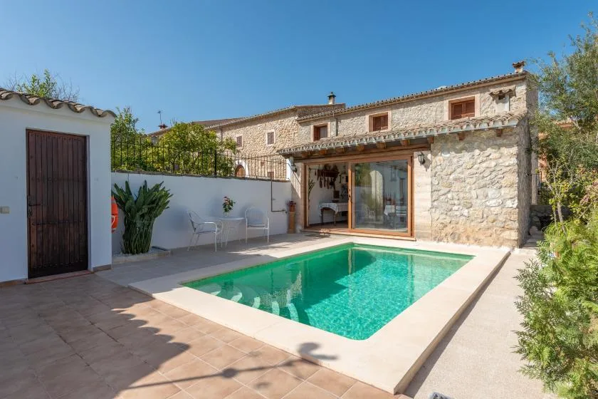 A swimming pool sits beside a stone house and a small paved patio.