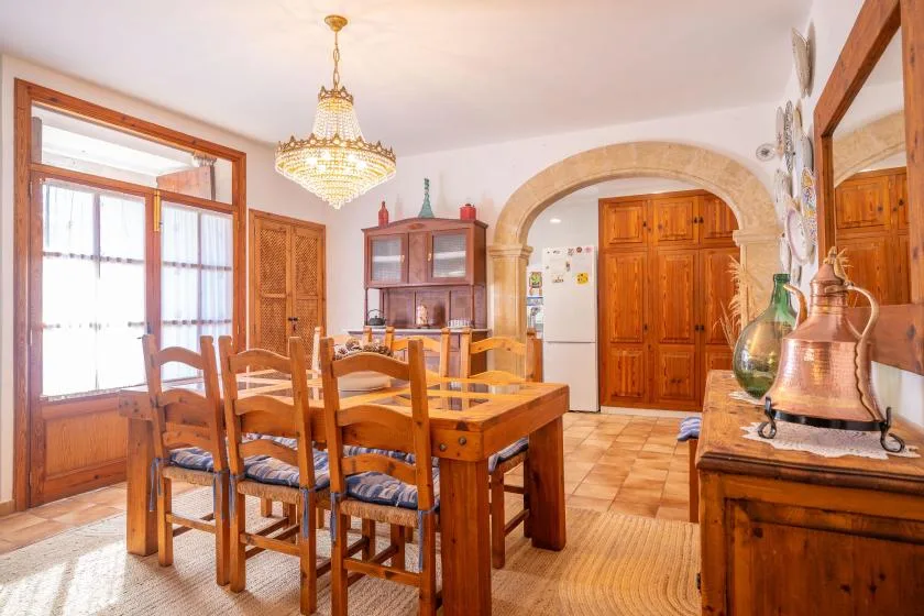 A wooden dining table and chairs fill a bright room with an arched doorway.