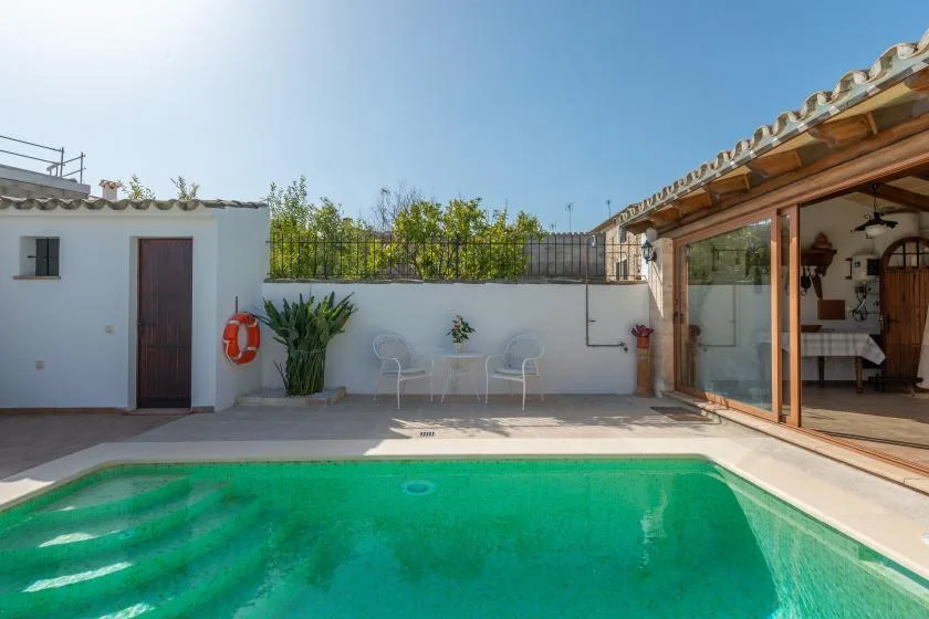 An outdoor swimming pool beside a patio and a glass-fronted room.