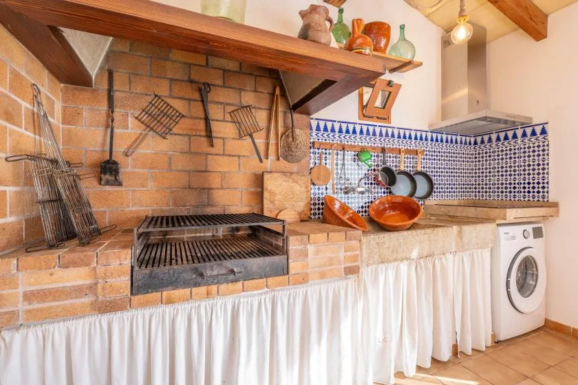 A rustic kitchen with a brick cooking area, tiled backsplash, and washing machine.