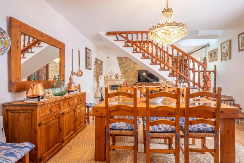 A wooden dining table and chairs sit beneath a staircase in a furnished dining room.
