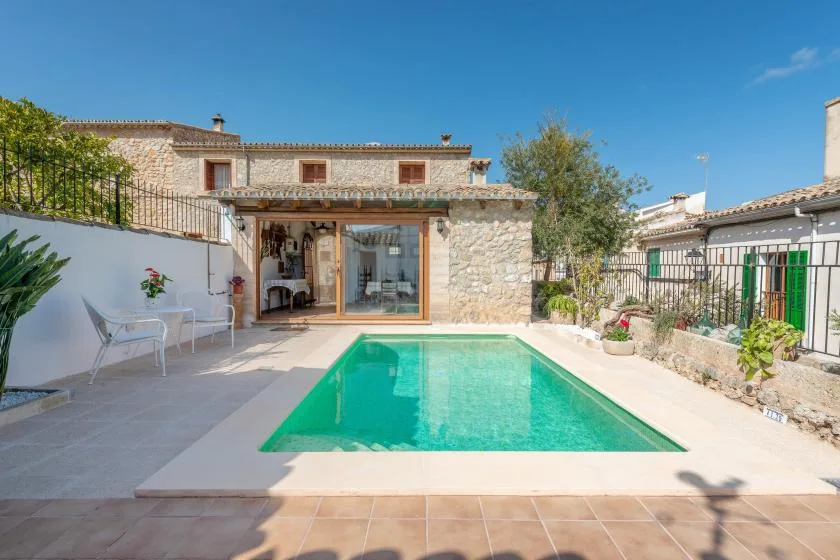 A courtyard pool sits beside a stone house and patio seating.