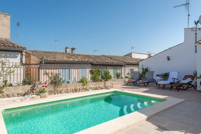 A swimming pool sits beside a paved patio with lounge seating and potted plants.