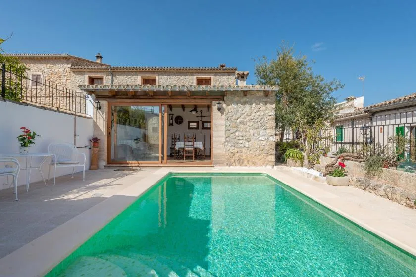 A swimming pool in front of a stone house with a covered patio.