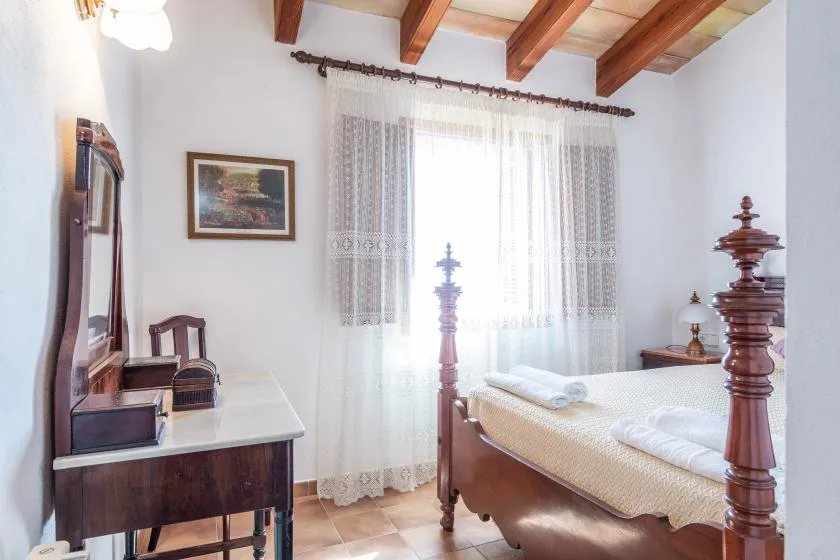 A bedroom with a wooden bed, lace curtains, and exposed ceiling beams.