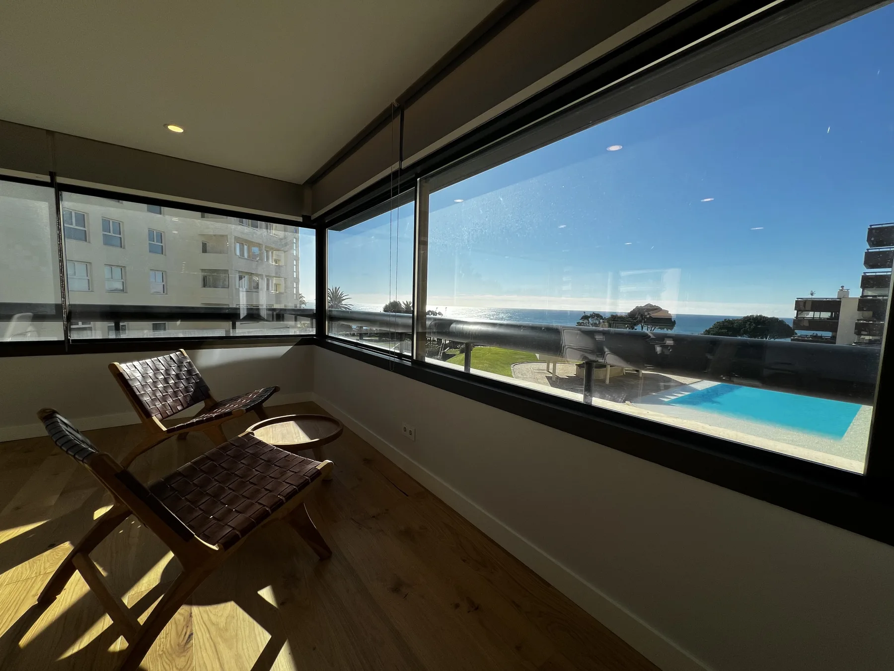 Una zona de estar soleada da al océano y a una piscina a través de grandes ventanas.