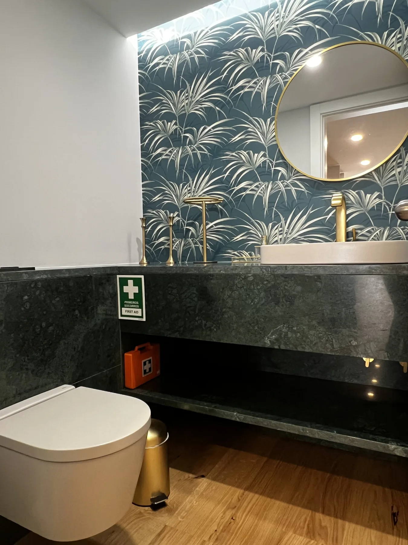 A bathroom with a wall-mounted toilet, dark counter, and patterned wallpaper.
