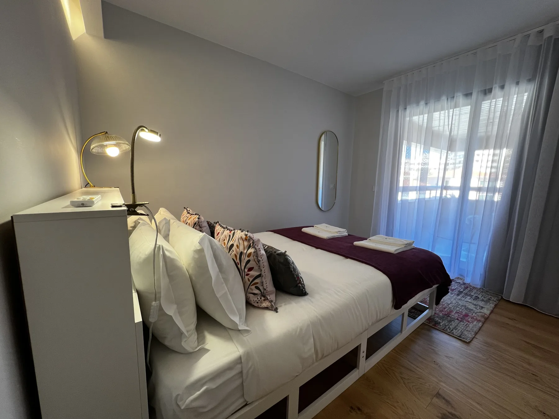 A bedroom with white bedding and a large curtained window.