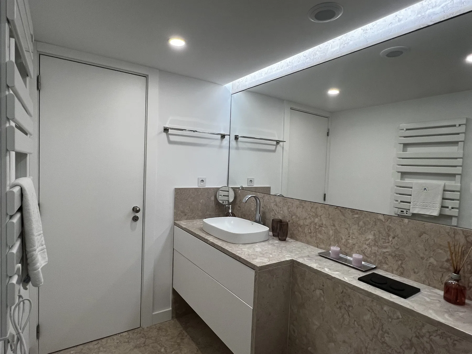 A modern bathroom with a long vanity, vessel sink, and wall-mounted towel warmer.