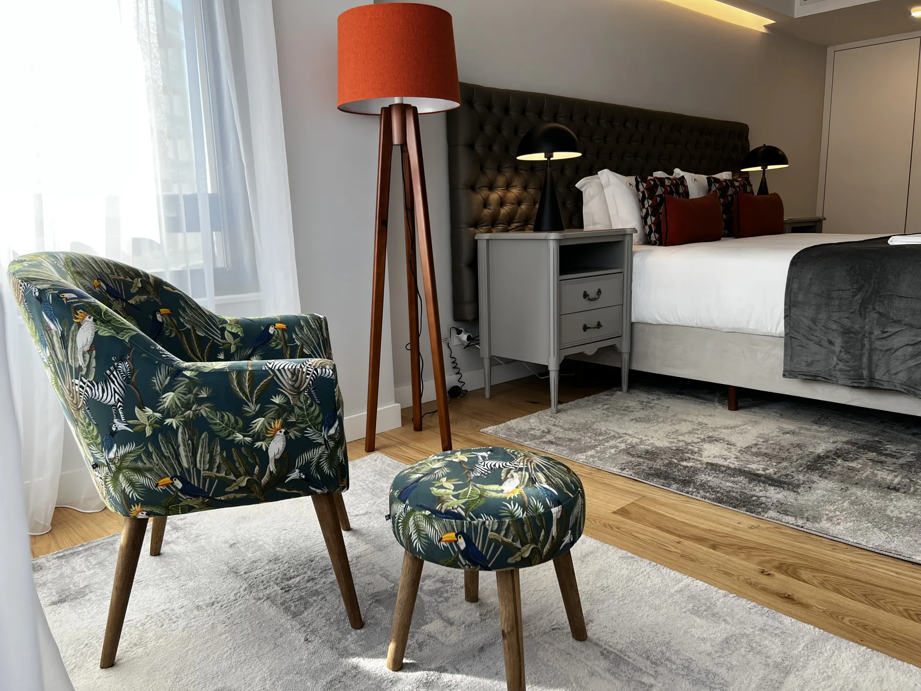 A bedroom with a bed, bedside table, and upholstered seating near a bright window.