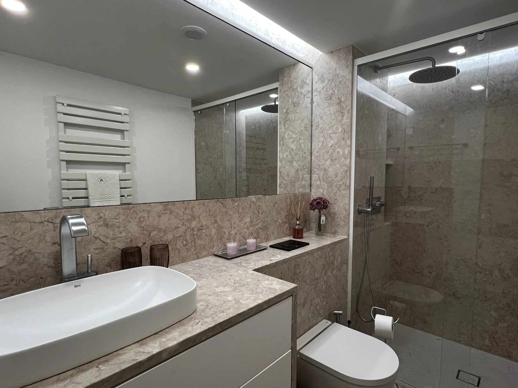 A modern bathroom with a stone countertop, sink, and glass shower.