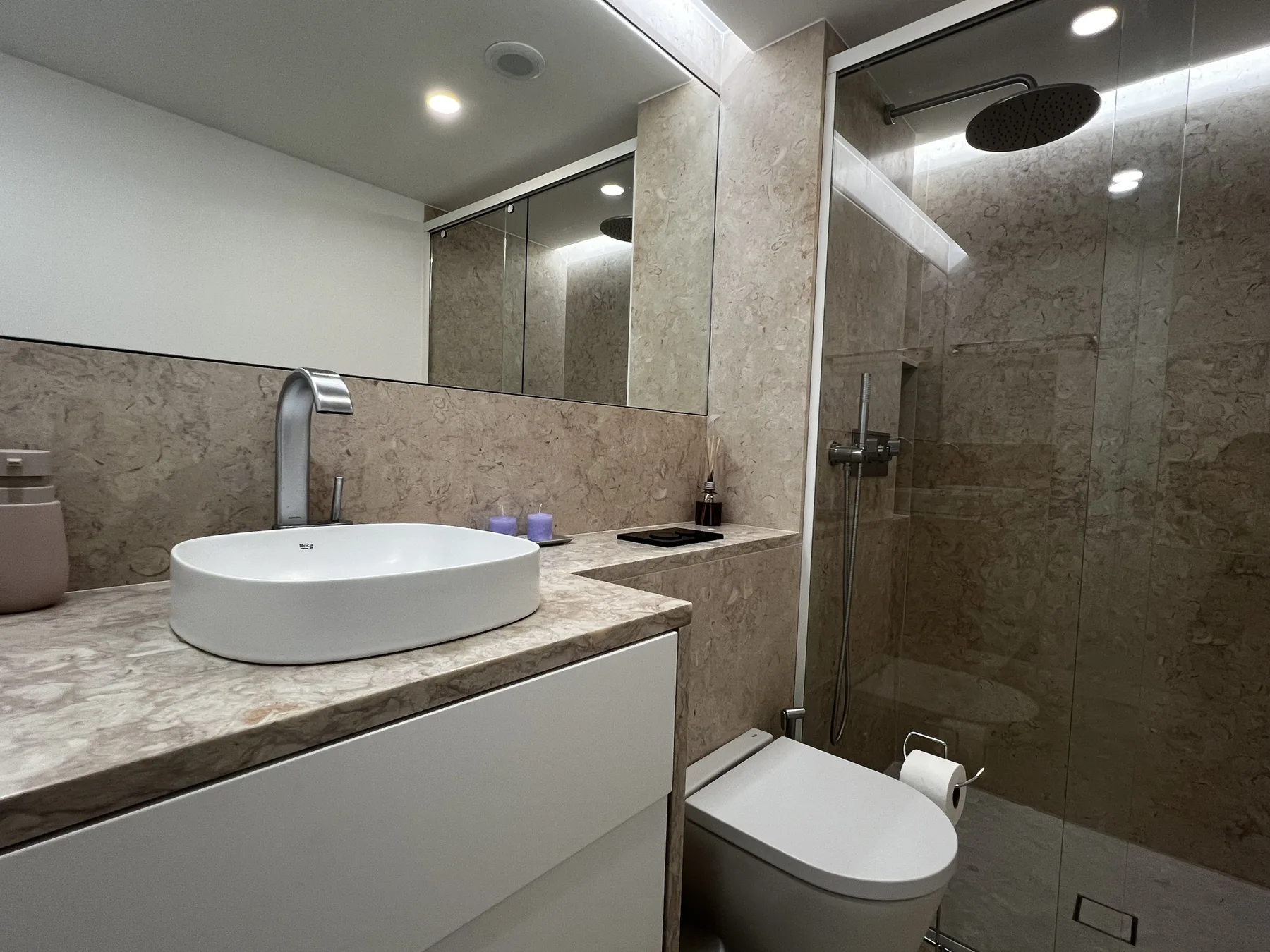 A bathroom with a basin, mirror, toilet, and shower.