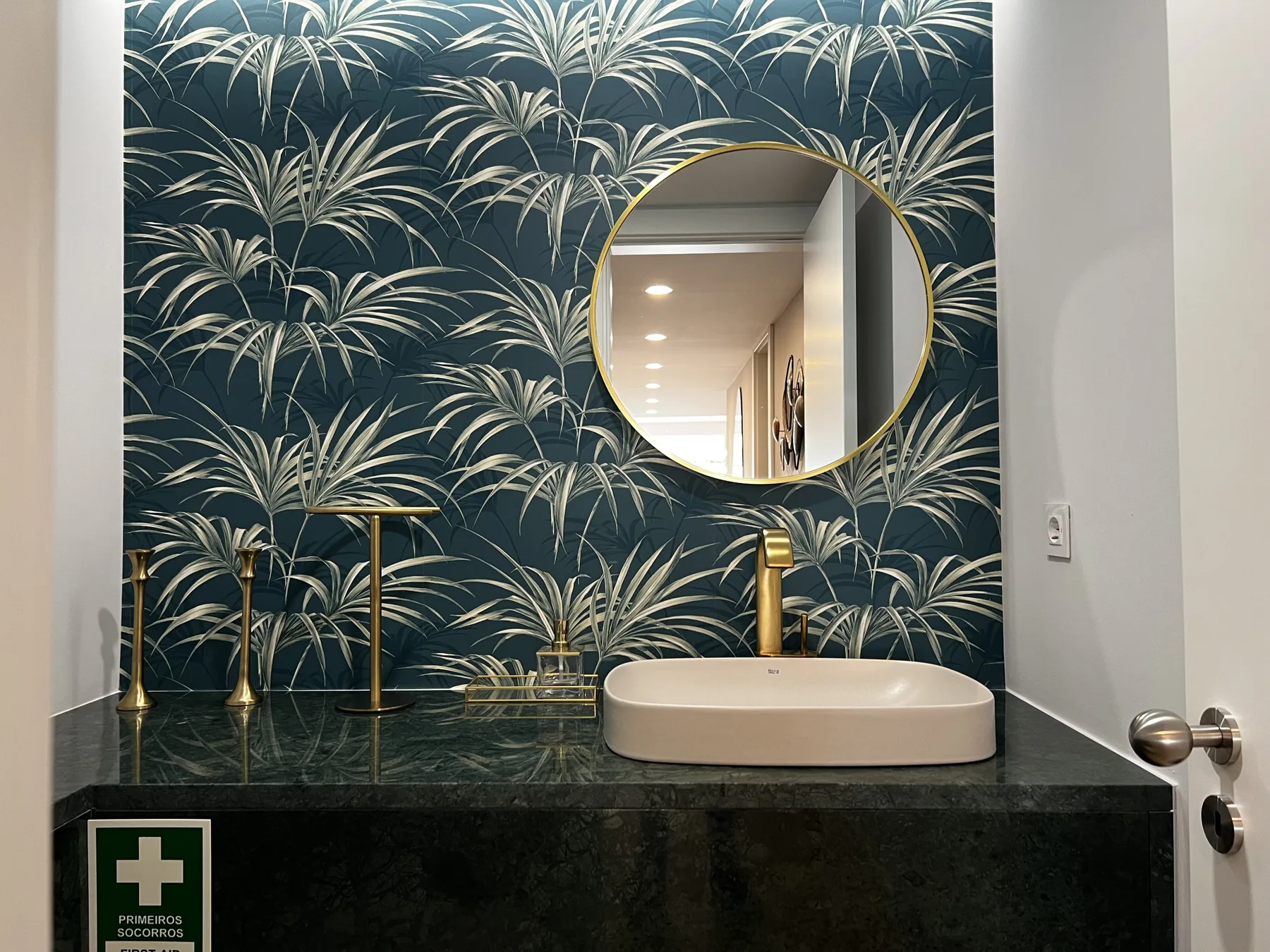 A bathroom vanity with a vessel sink stands against dark botanical wallpaper.