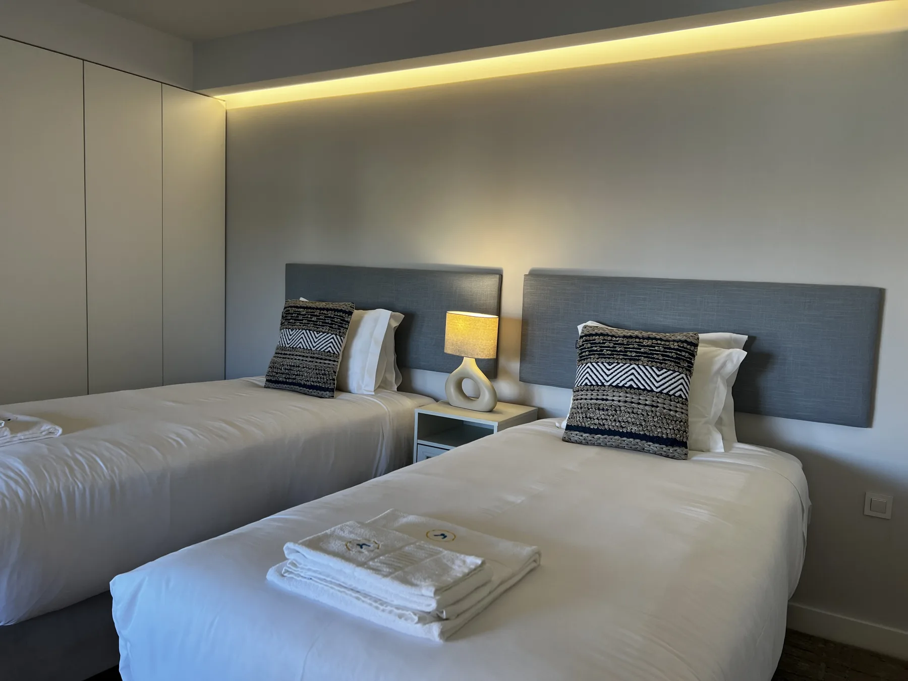 A bedroom with two beds and folded towels on one bed.