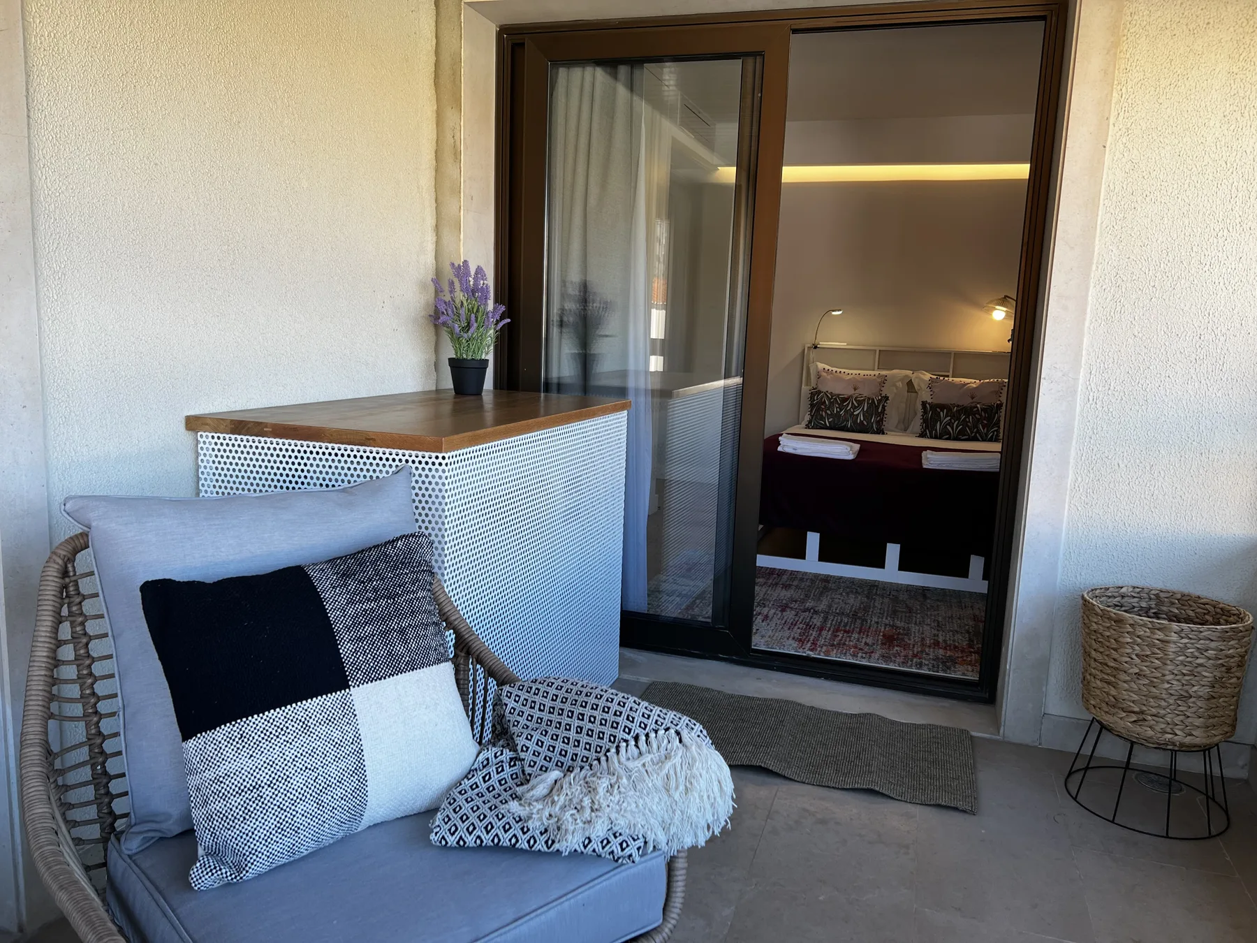 A furnished balcony opens onto a bedroom through a sliding glass door.