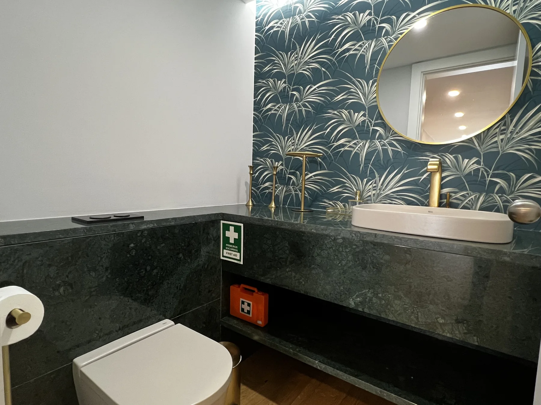 A bathroom vanity with a round mirror and a patterned wall.