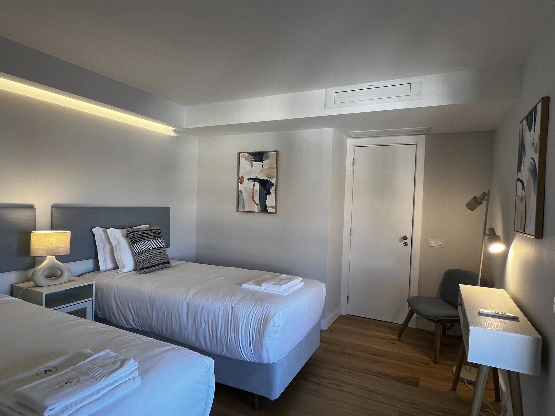 A bedroom with two beds, framed artwork, and a small desk.
