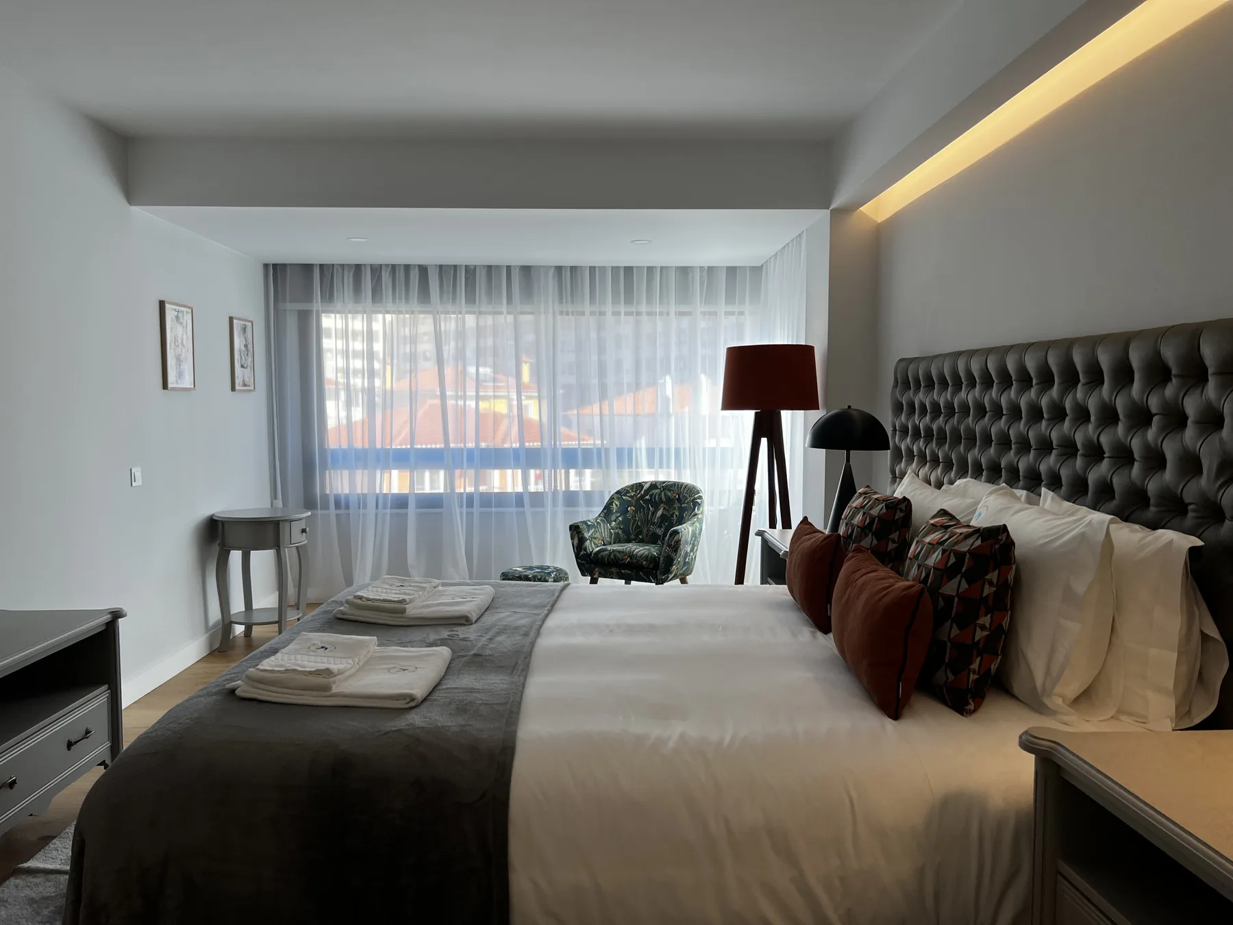 A bedroom with a large bed, patterned pillows, and a curtained window.