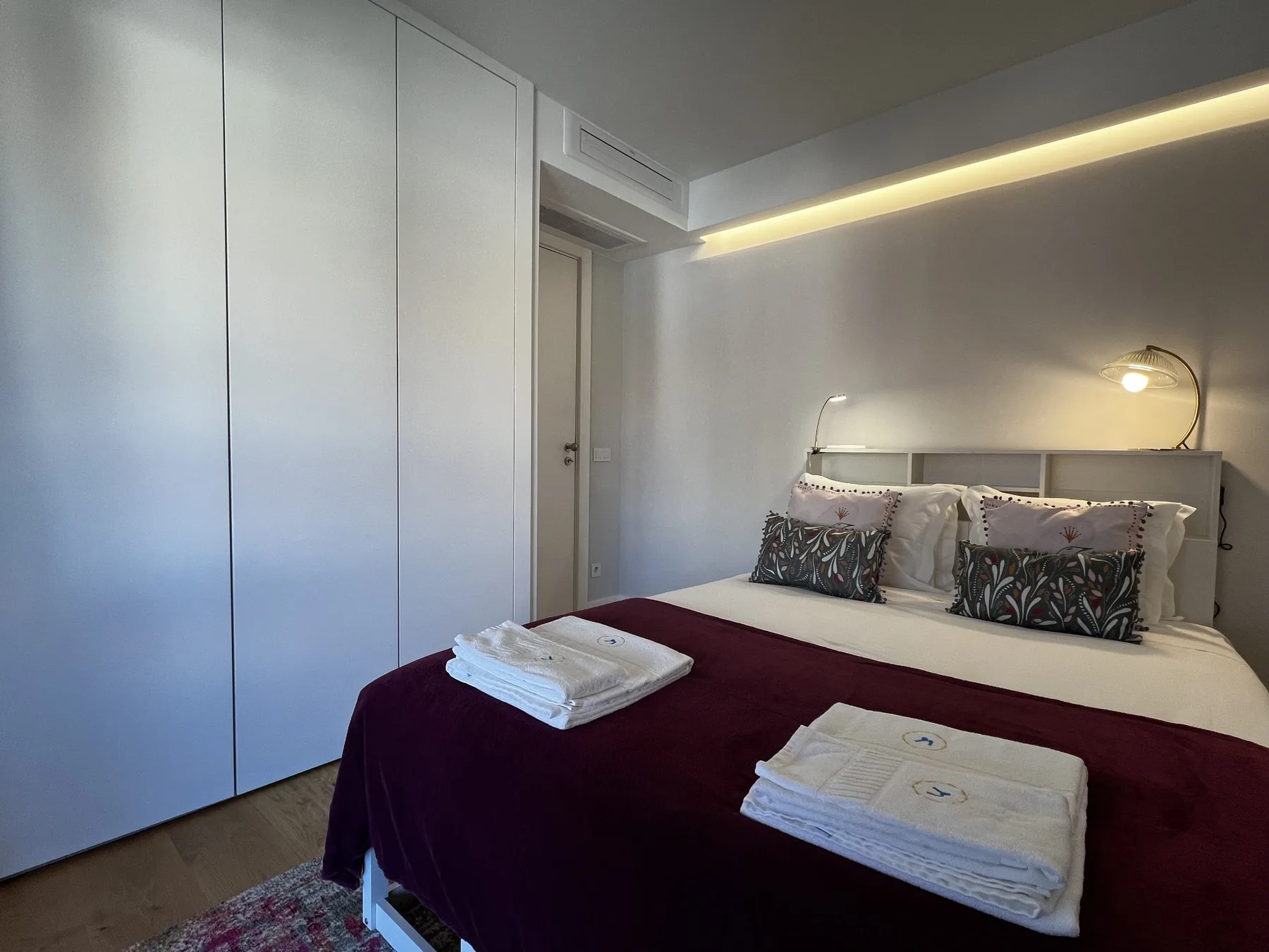 A bedroom with a bed, folded towels, and built-in wardrobes.