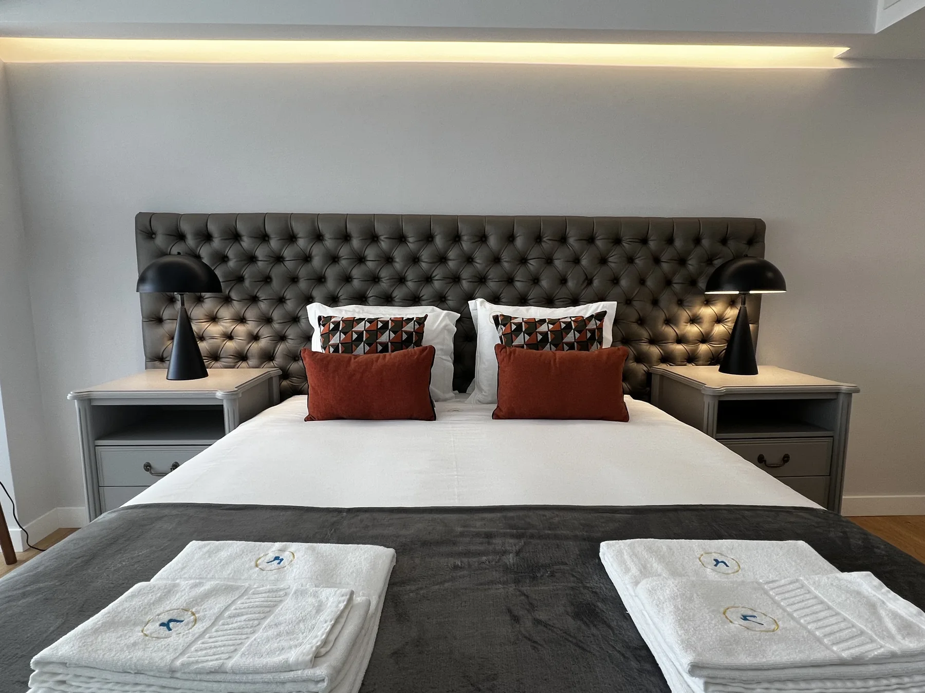 A bedroom with a neatly made bed, tufted headboard, and matching bedside tables.