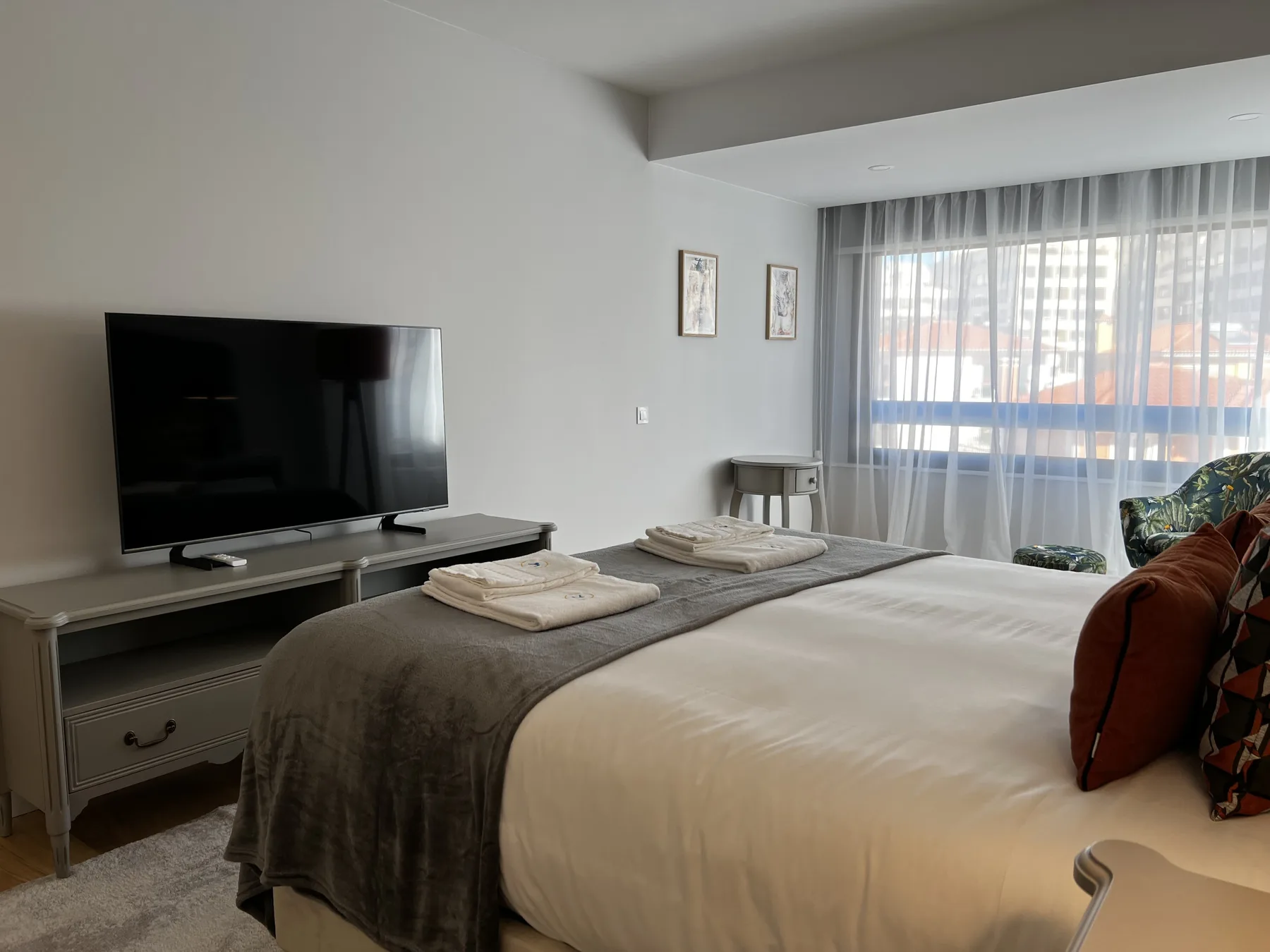 A bedroom with a neatly made bed, folded towels, and a television on a console.