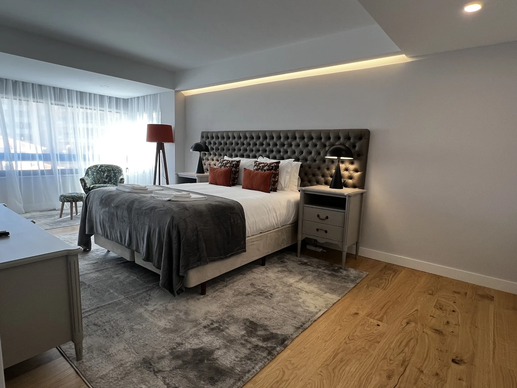 A bedroom with a large bed, bedside tables, and a window with sheer curtains.