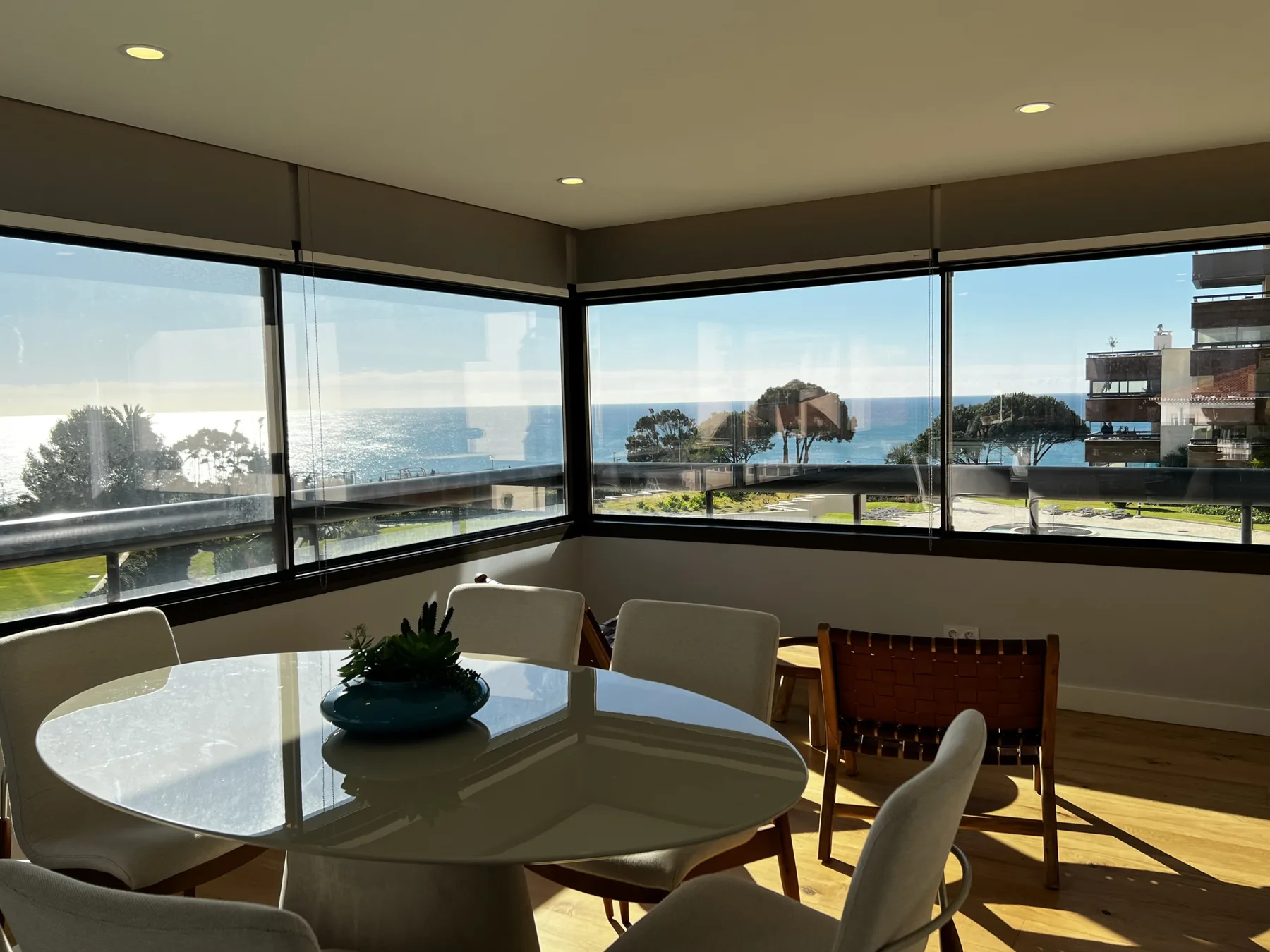 A dining area with a round table and wide windows overlooking the sea.