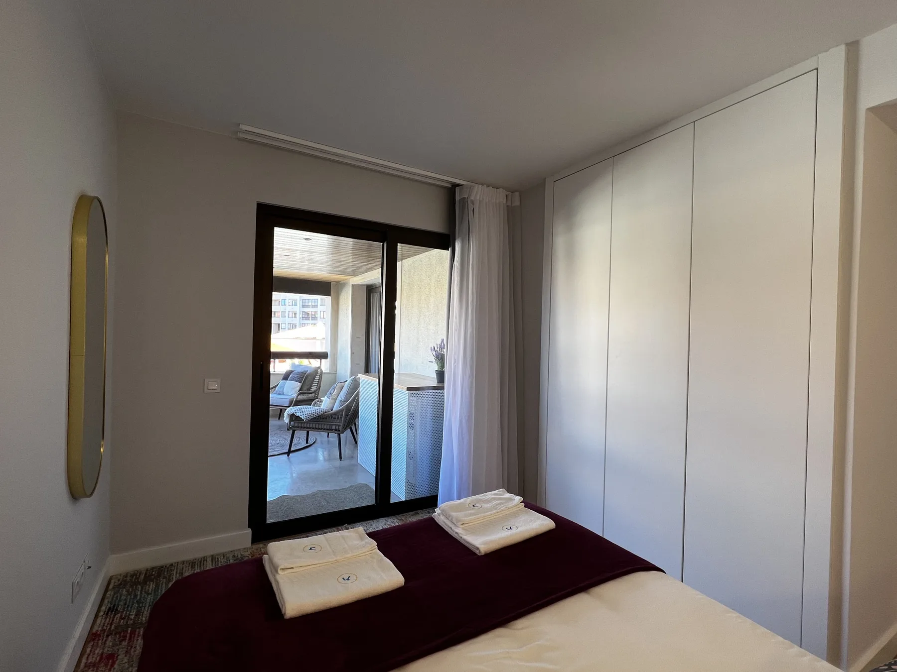 A bedroom with a bed and folded towels beside a glass door.