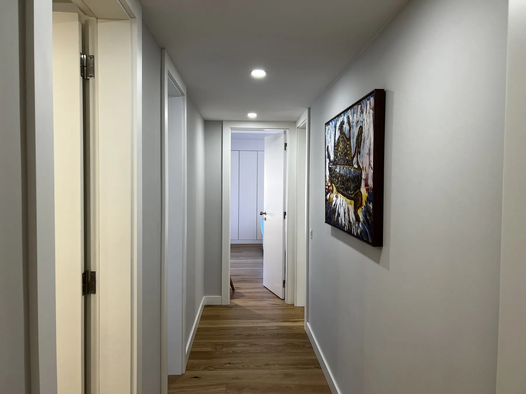 A hallway with wood flooring and framed artwork on the wall.