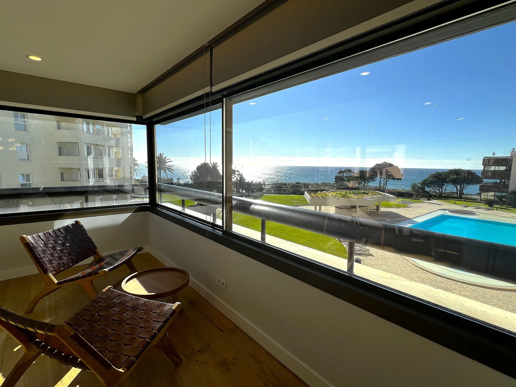A glazed sitting area overlooks a swimming pool and the ocean.