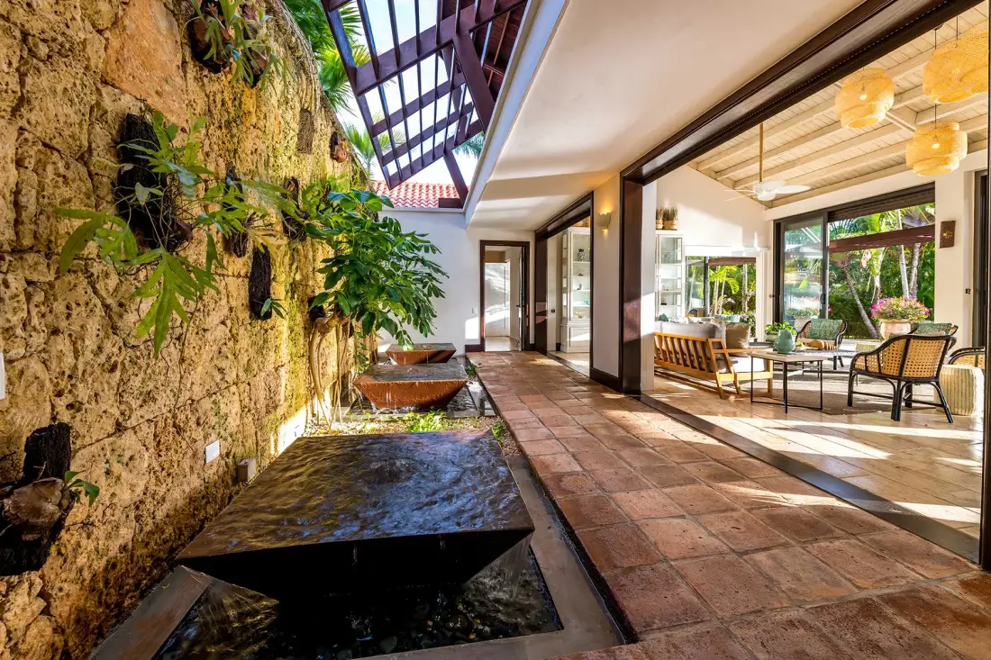 Un comedor luminoso y abierto junto a un muro de piedra con plantas y una fuente baja.