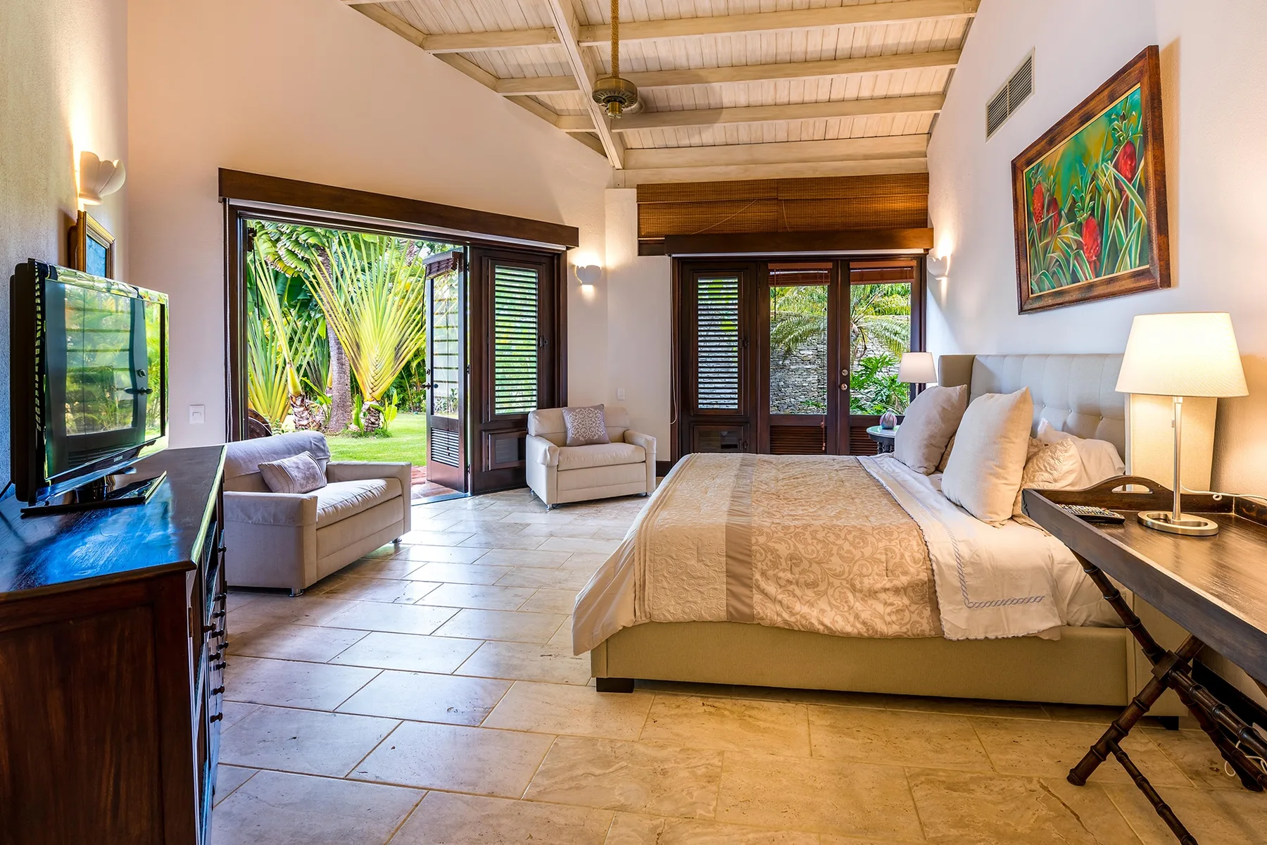 Dormitorio con una cama grande, asientos y puertas de vidrio que dan a la vegetación.