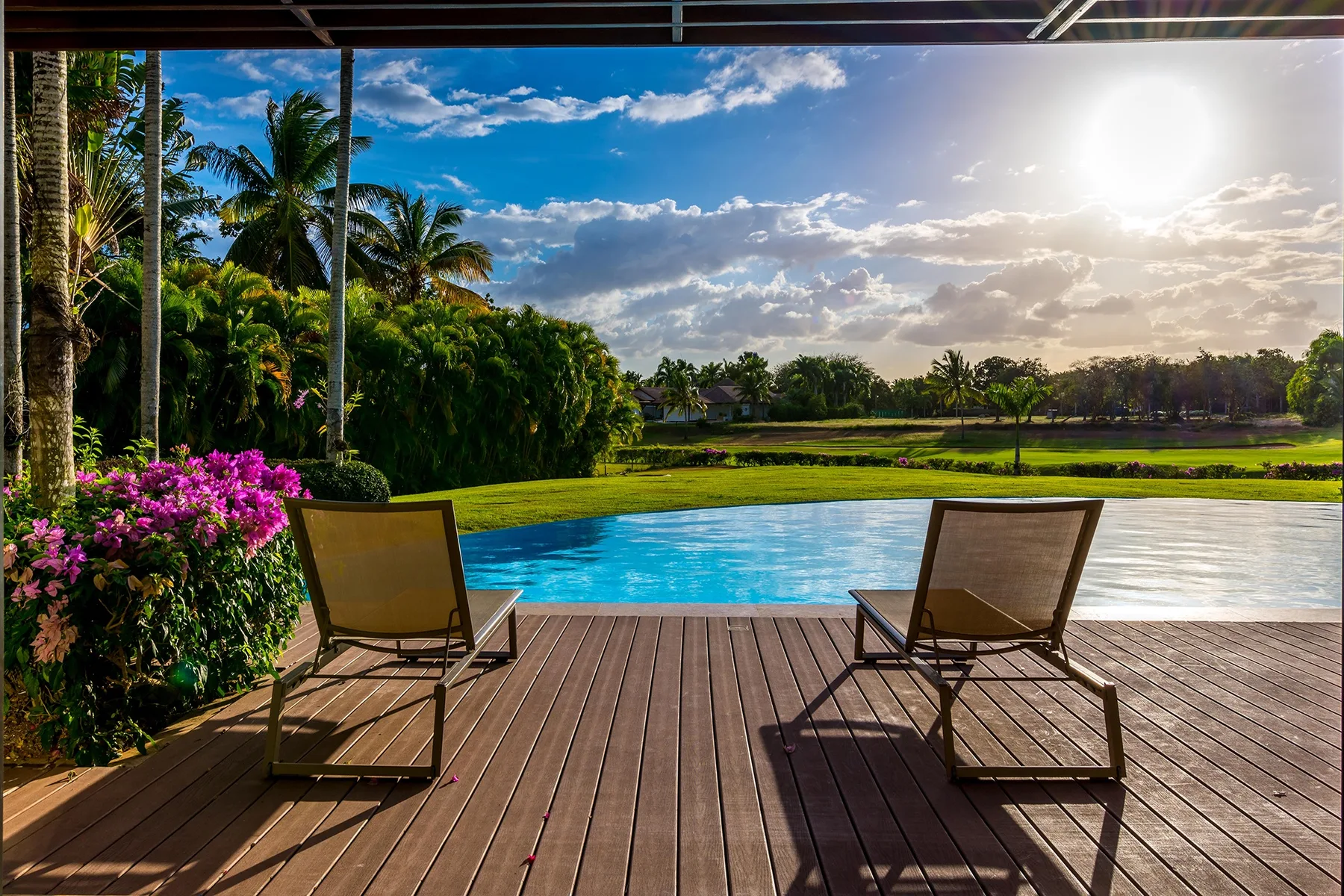 Una terraza junto a la piscina da a un paisaje verde, con dos tumbonas al sol.
