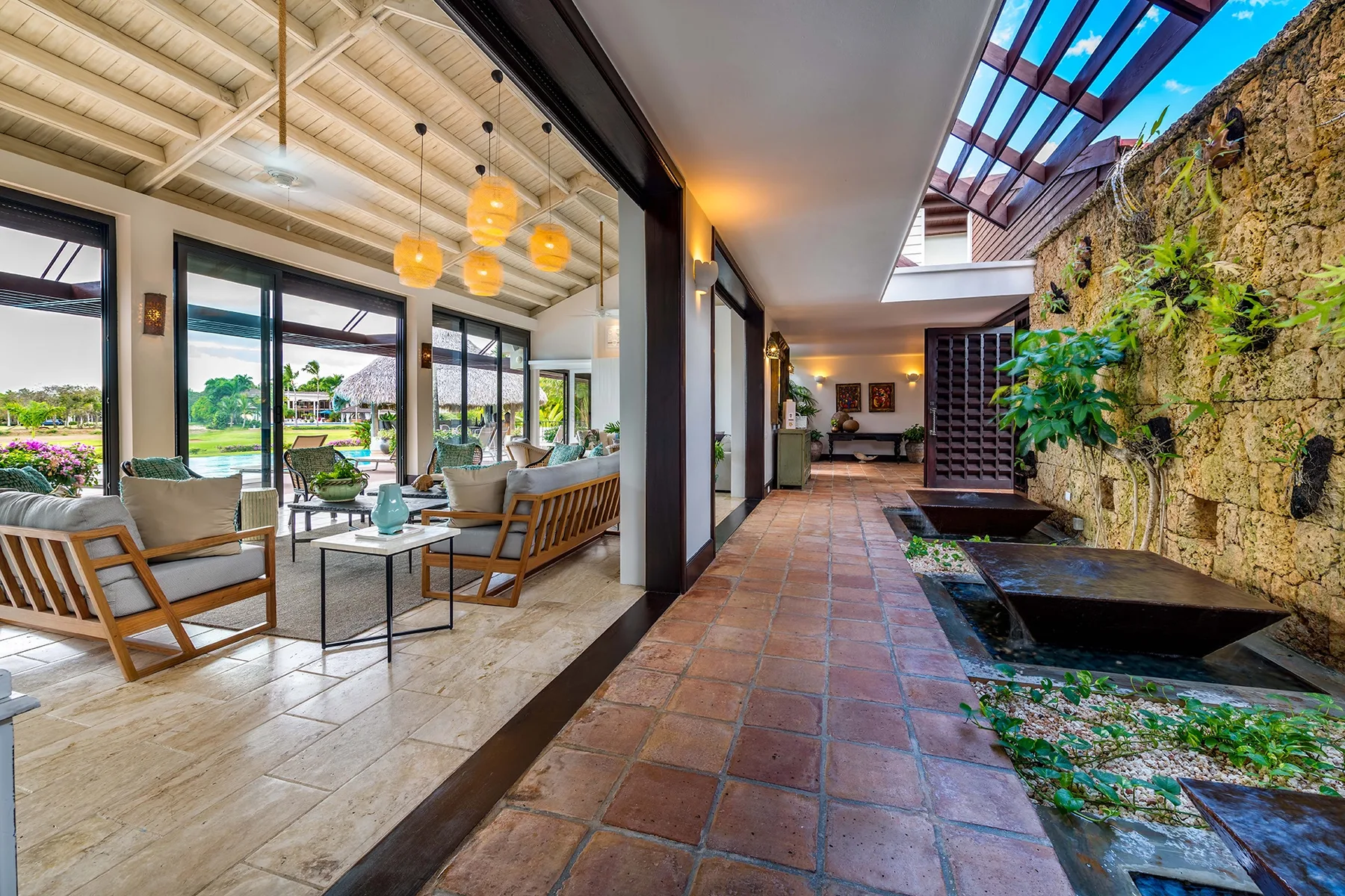 Una sala luminosa se abre a un patio embaldosado con un muro de piedra con plantas.