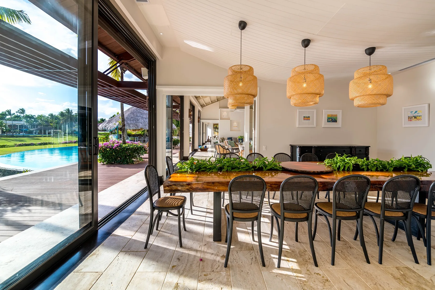 Comedor con una larga mesa de madera junto a grandes ventanales con vistas a una piscina.