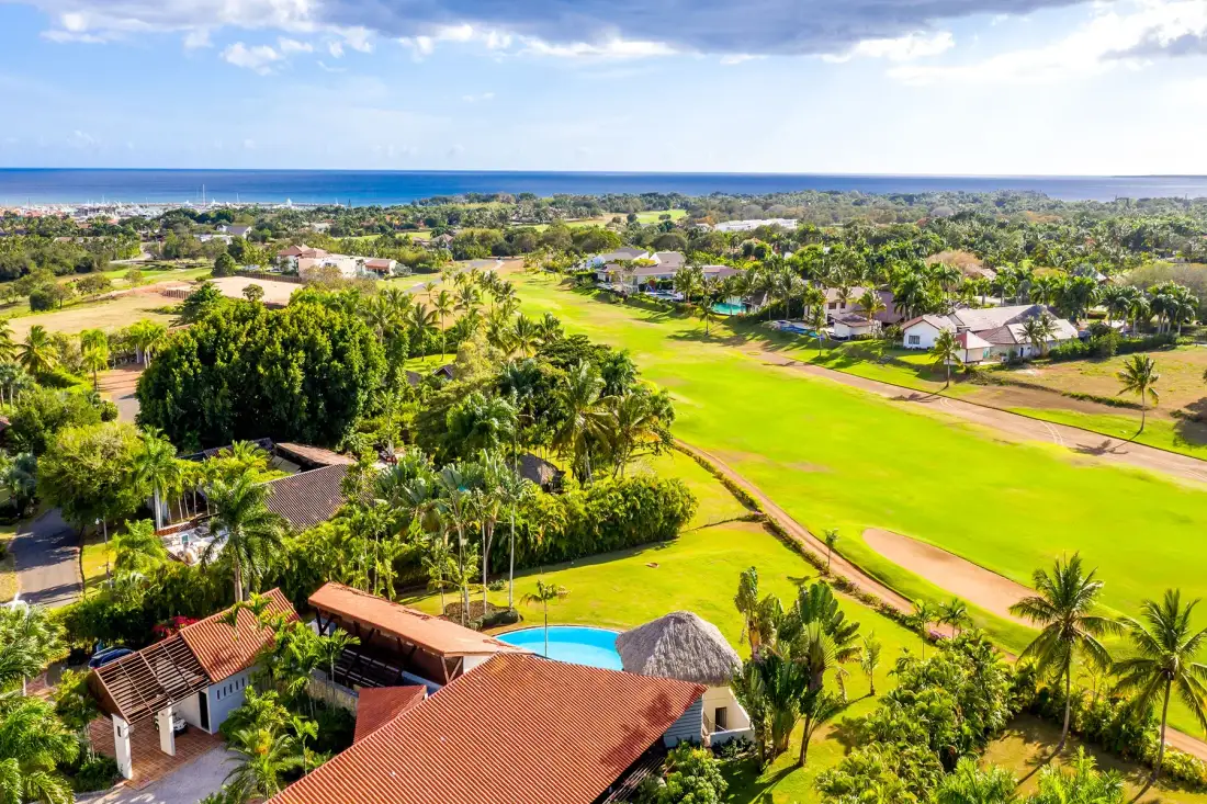 Vista aérea de un campo de golf tropical con casas y el océano a lo lejos.
