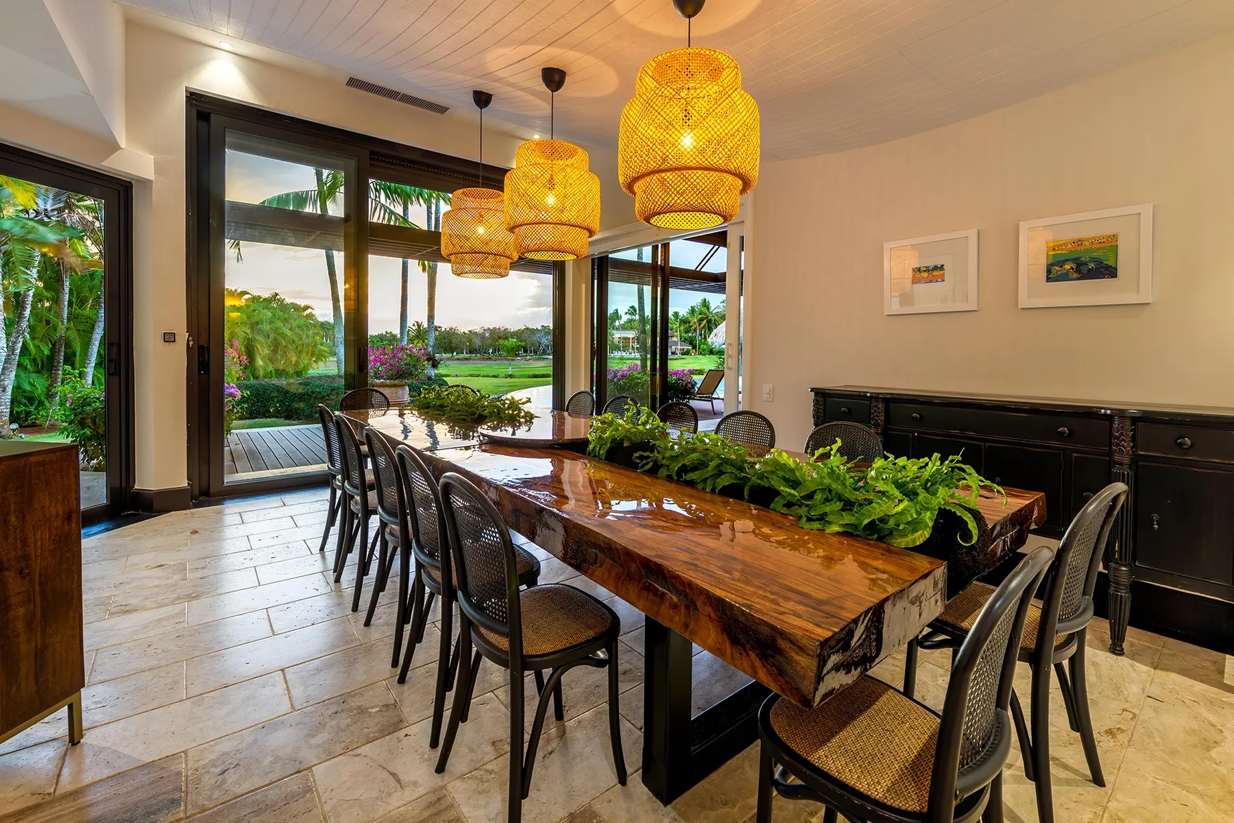 Comedor con una larga mesa de madera, asientos oscuros y grandes ventanas con vistas a la vegetación.