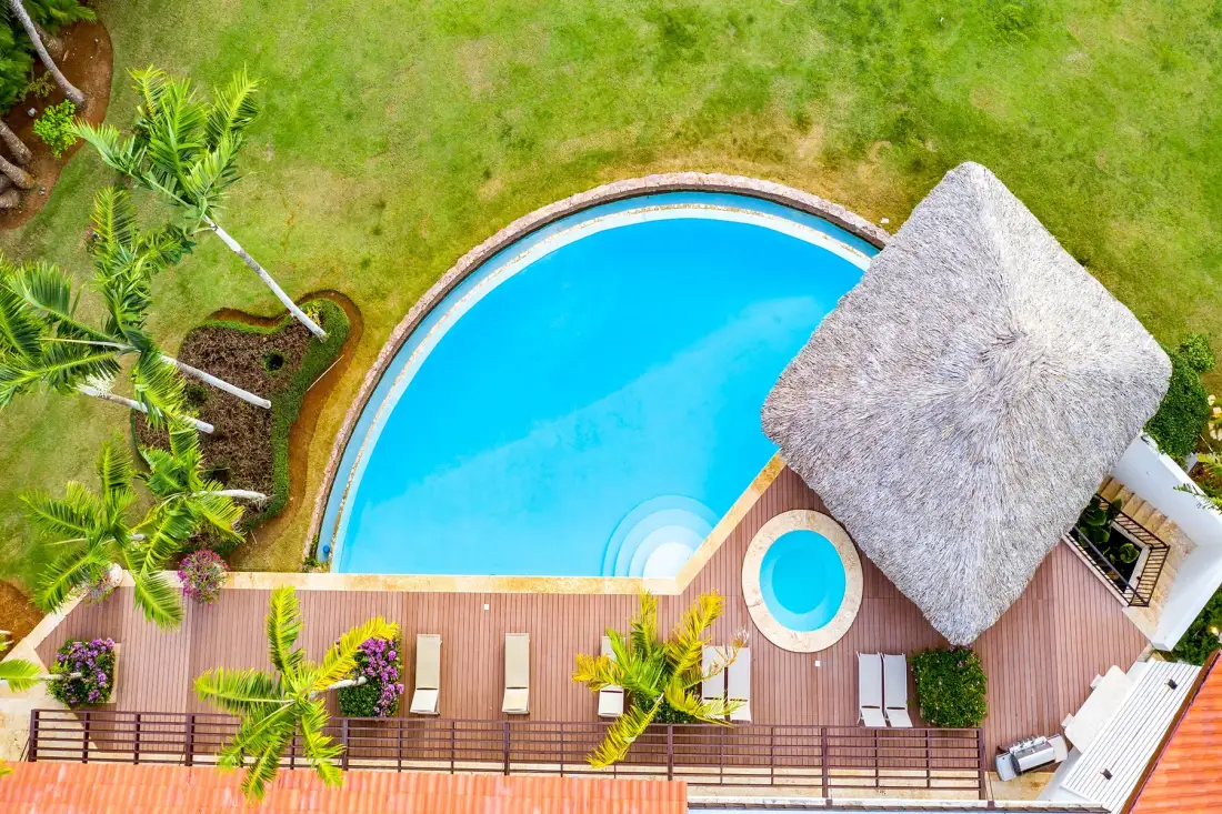 Vista aérea de una piscina junto a una terraza de madera y un pabellón con techo de paja.