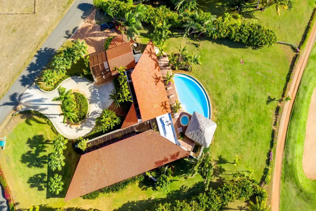 Vista aérea de una casa, una piscina curva y un jardín cuidado.