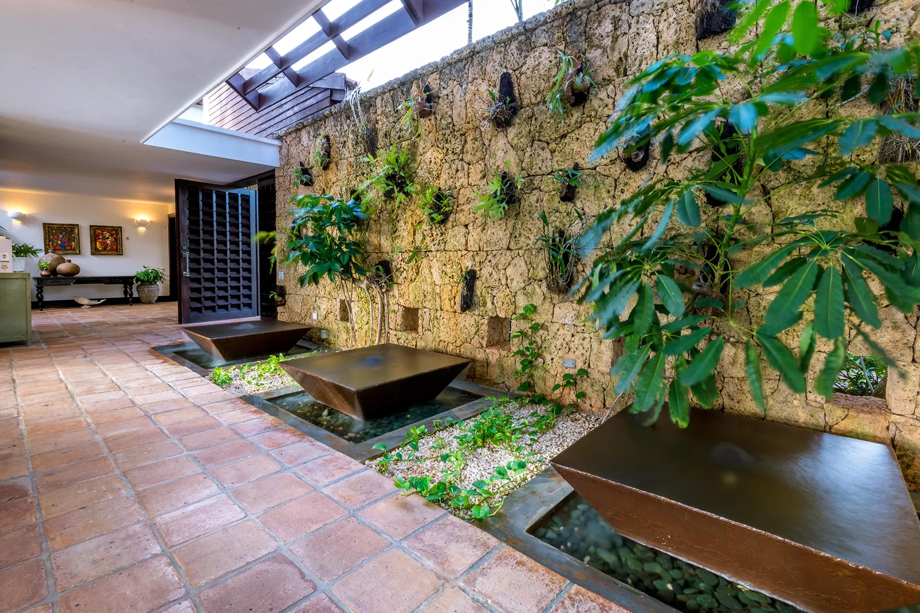 Un sendero de patio embaldosado bordea estanques poco profundos y un muro de piedra con plantas.